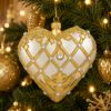 Elegant ivory and gold heart Christmas ornament hanging on a decorated Christmas tree with warm lights