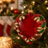 Red jeweled heart glass Christmas ornament hanging on a Christmas tree with warm lights, pearl accents, green leaves and gold detailing